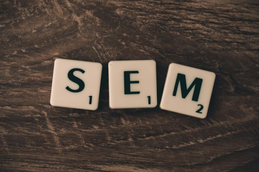 Klocki z literami SEM na drewnianym tle – ilustracja do tematu junior marketing specialist zarobki i pracy w marketingu internetowym.